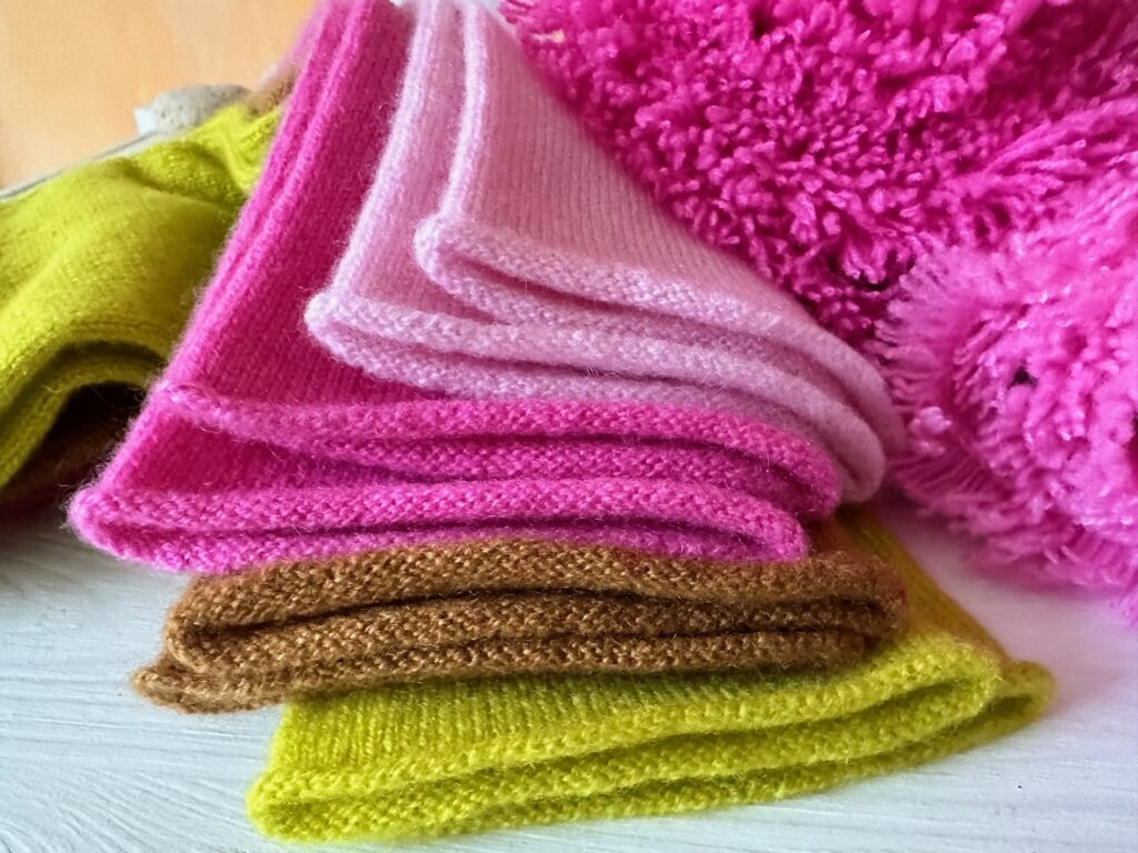 Cashmere-Modelle in schönen Farben (rosa, pink, senfgelb und zimt), abgebildet sind Accessoires, Armlinge (Stulpen), und eine Fransenkante von einer grossen Stola