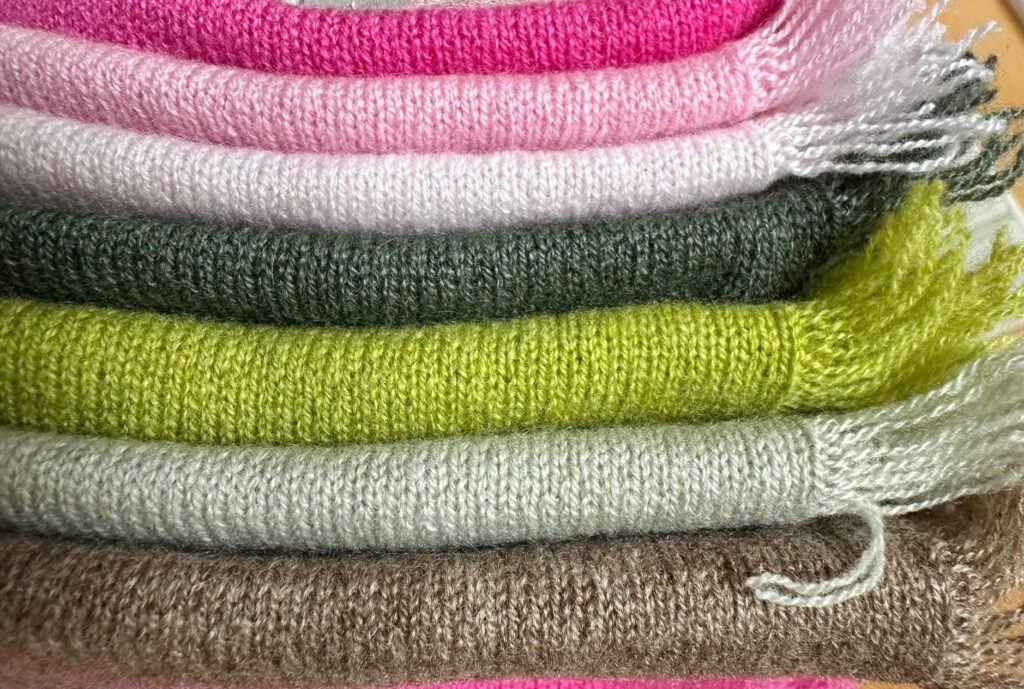 Cashmere-Hals-Tuecher gestrickt, übereinandergestapelt in unterschiedlichen Farben (hellrosa, rosa, pink, grüntoenen, beigebraun) mit an der Seite sichtbarer Fransenkante,