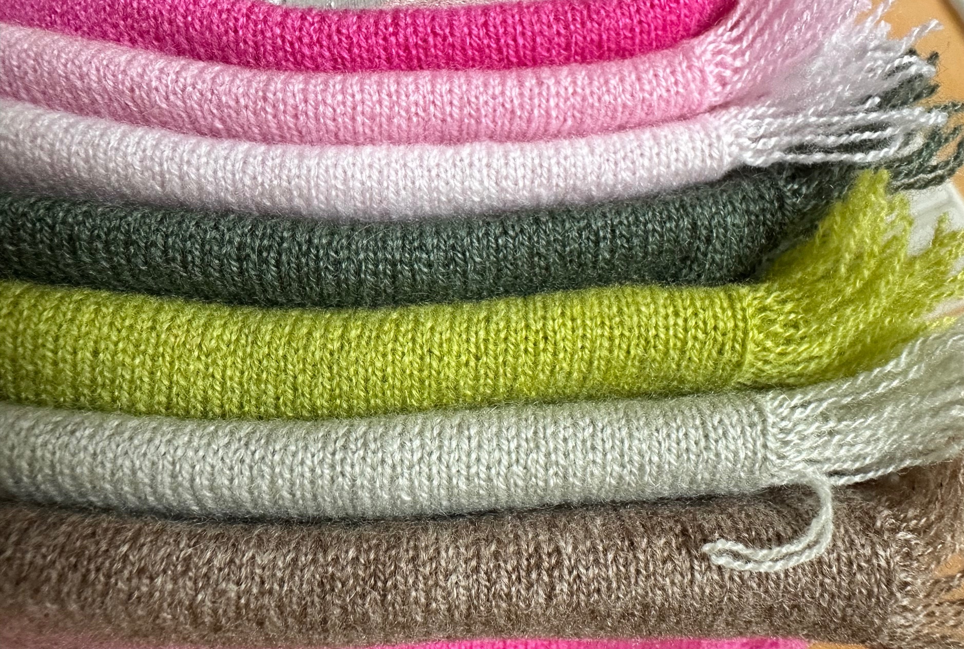 Cashmere-Hals-Tuecher gestrickt, übereinandergestapelt in unterschiedlichen Farben (hellrosa, rosa, pink, grüntoenen, beigebraun) mit an der Seite sichtbarer Fransenkante,